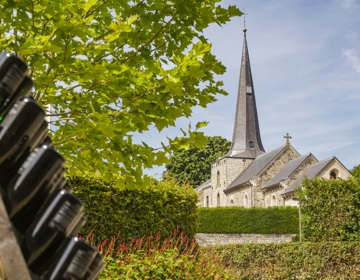 De kerk van Holset op een zonnige dag met een rek met wijnflessen op de voorgrond