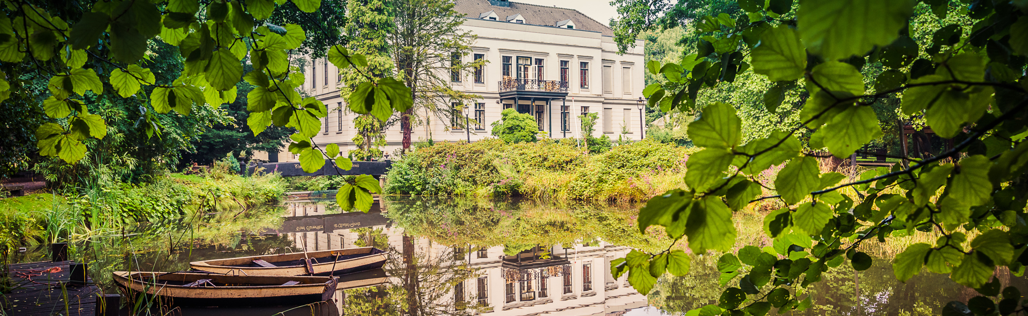 Vooraanzicht van Kasteel De Berckt in Baarlo. Voor het kasteel loopt een beekje en hier liggen twee roeiboten in