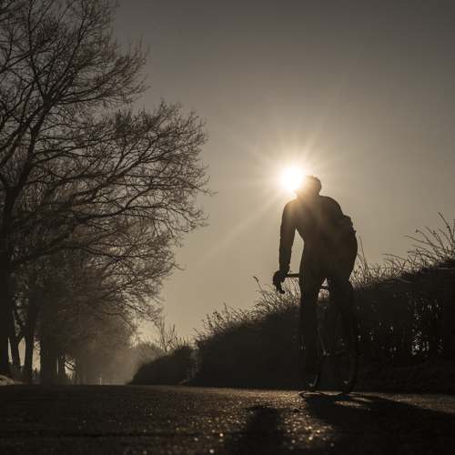 Wielrenner fietst met een laagstaande winterzon over een bevroren pad.