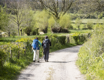 Twee dames met backpack wandelen over een onverharde weg richting de heuvels