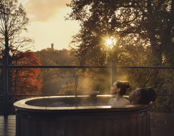 Twee dames in privé bubbelbad met uitzicht over de herfstige kleuren van de bomen. 