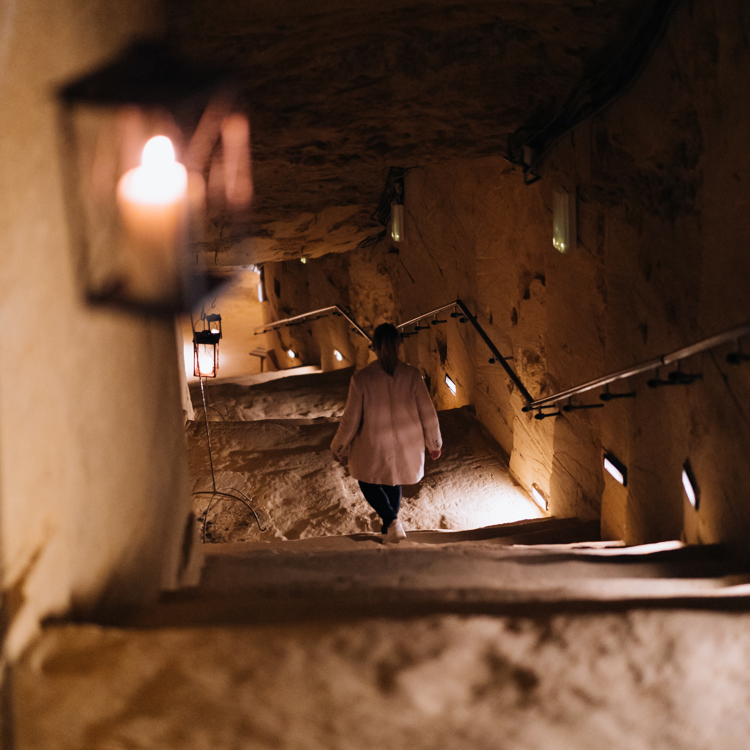 vrouw loopt een trap af in een grot met aan beide kanten lampjes.