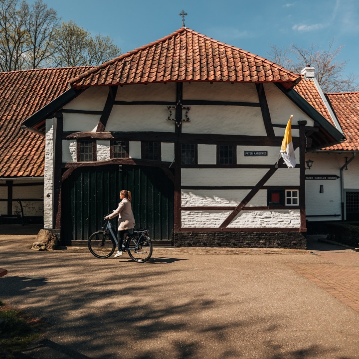 Een meisje fietst langs de oude poort van de Pater Karel Kapel