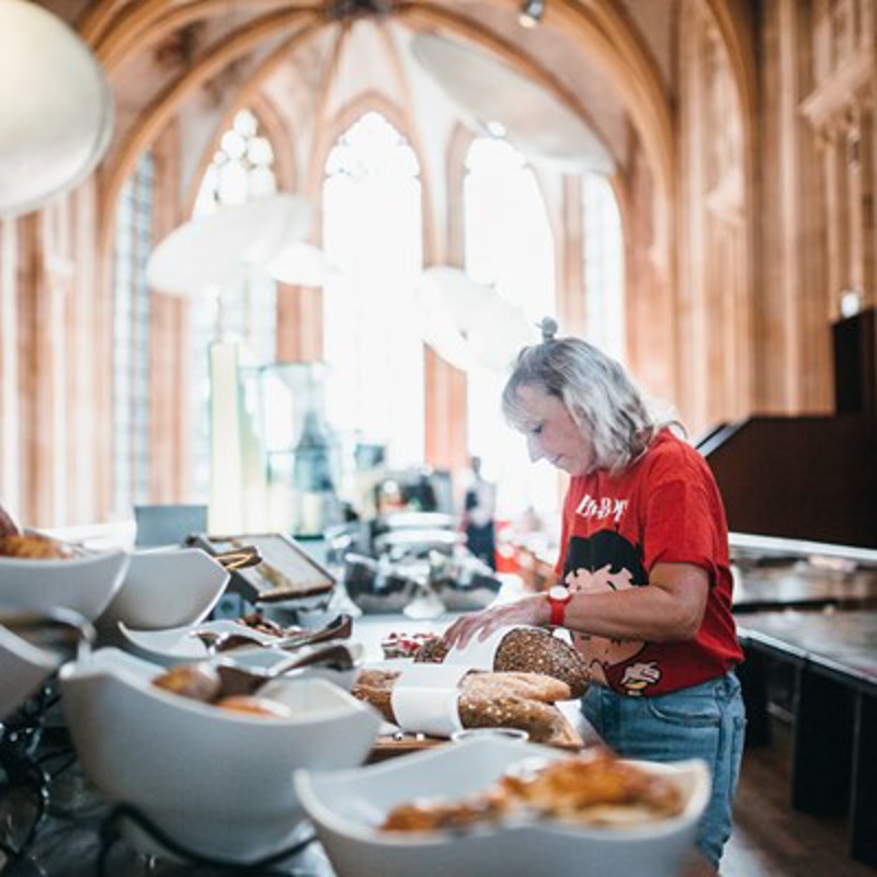 Vrouw snijdt een stukje brood af bij het ontbijt in een luxe hotel gelegen in een kerk. 