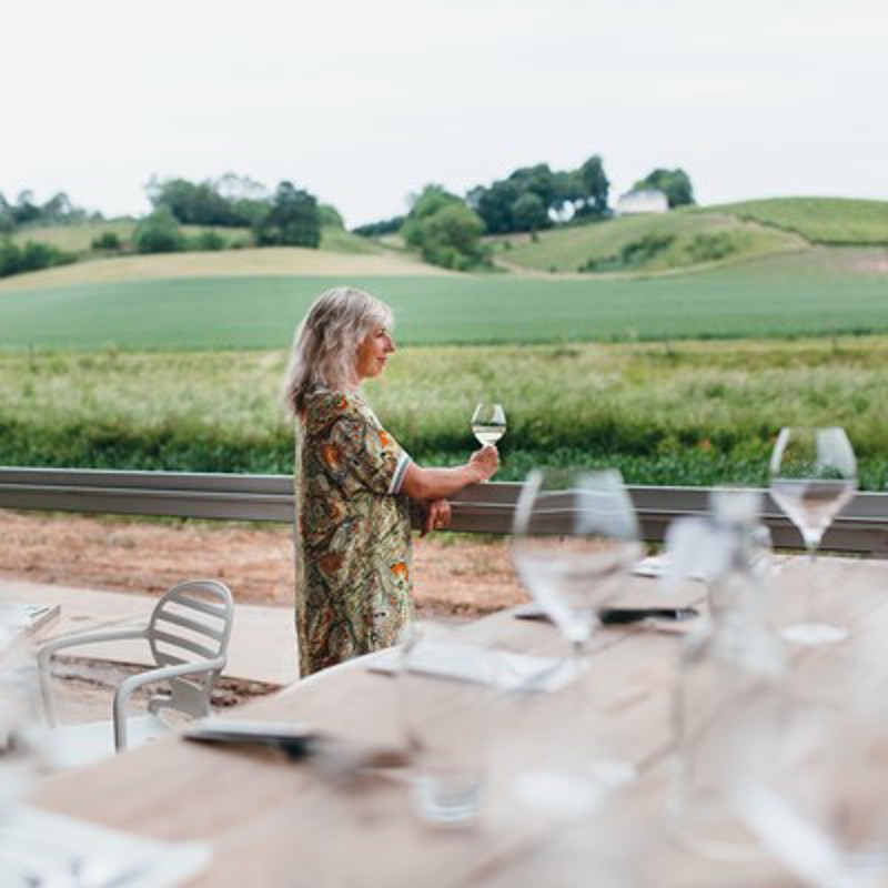 Vrouw staat met glas wijn in de land bij een reling en kijkt uit over Limburgs landschap. 