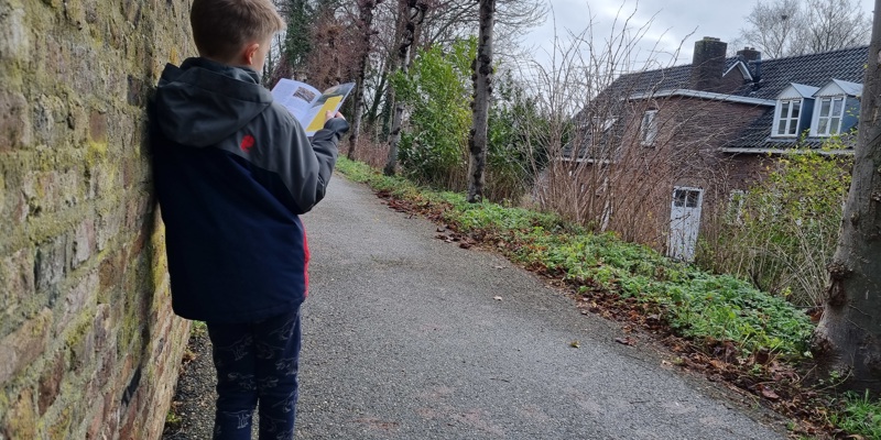 Kind kijkend in de stadswandeling brochure Sittard leunend tegen de stadsmuur op de oude stadswal