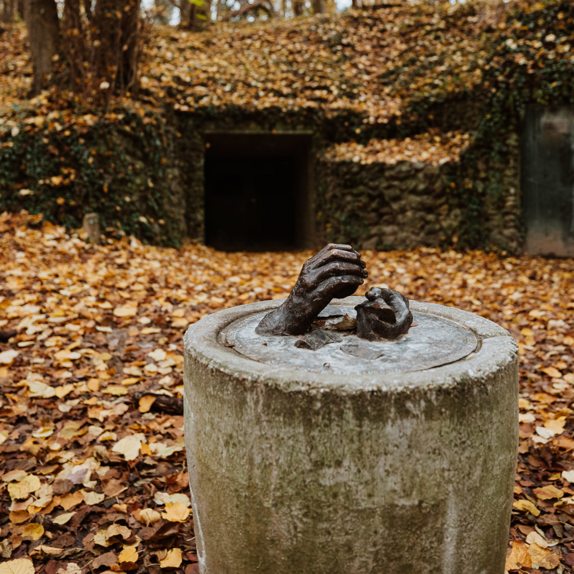 Een beeldhouwwerk met twee handen die vuursteen vasthouden in het bos voor de ingang van de vuursteenmijn 