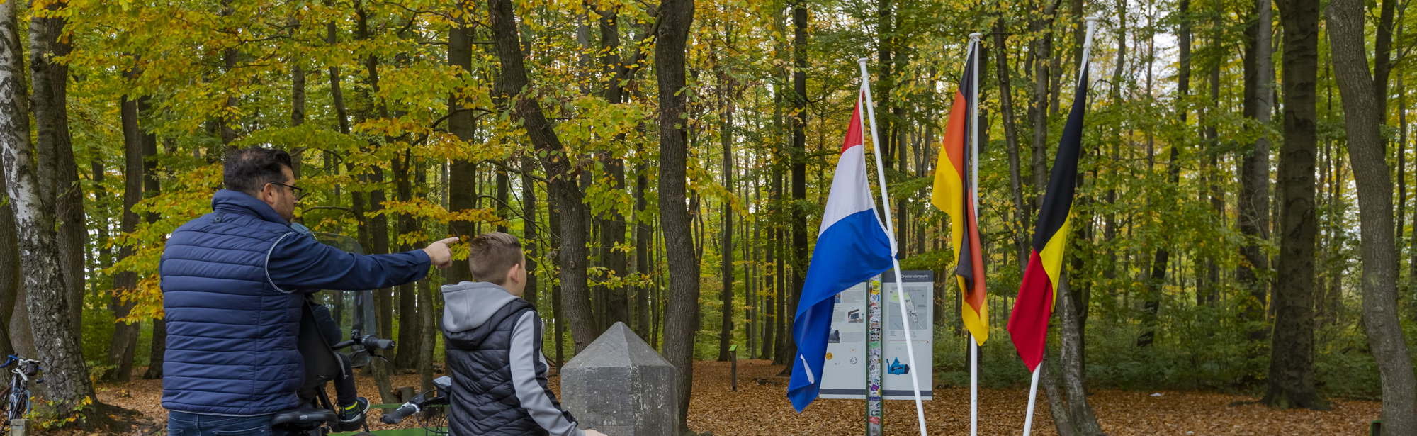 Een vader en zoon wijzen naar de drie nationale vlaggen op het Drielandenpunt