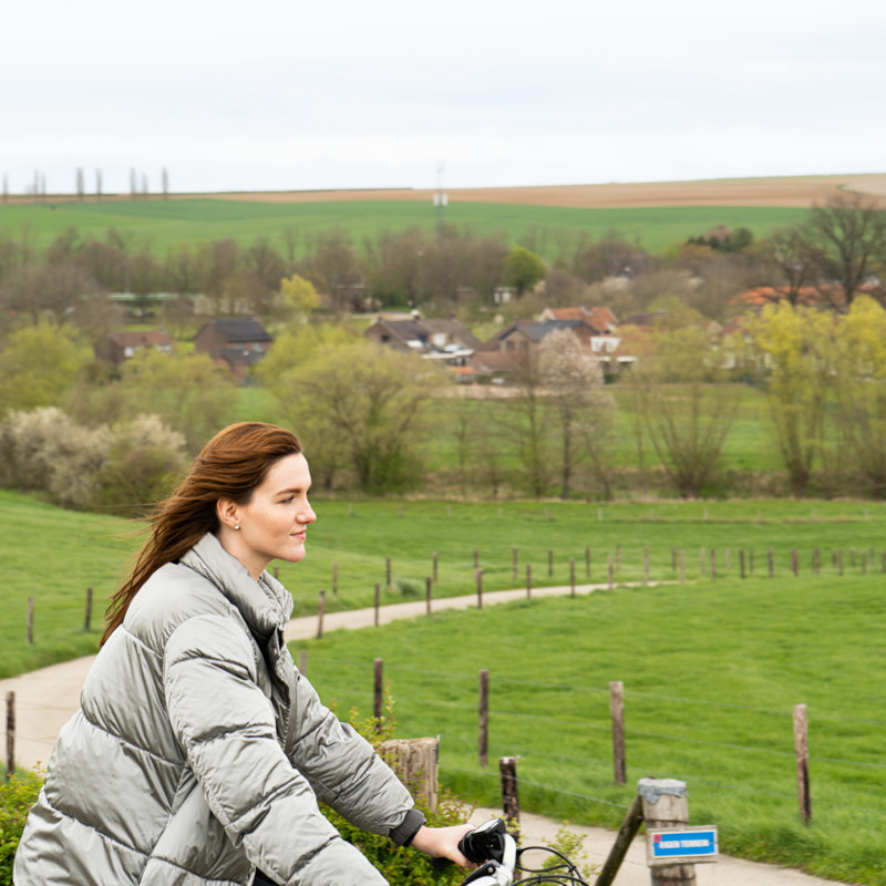 Een vrouw fietst over een pad met op de achtergrond een Zuid-Limburgs dorpje