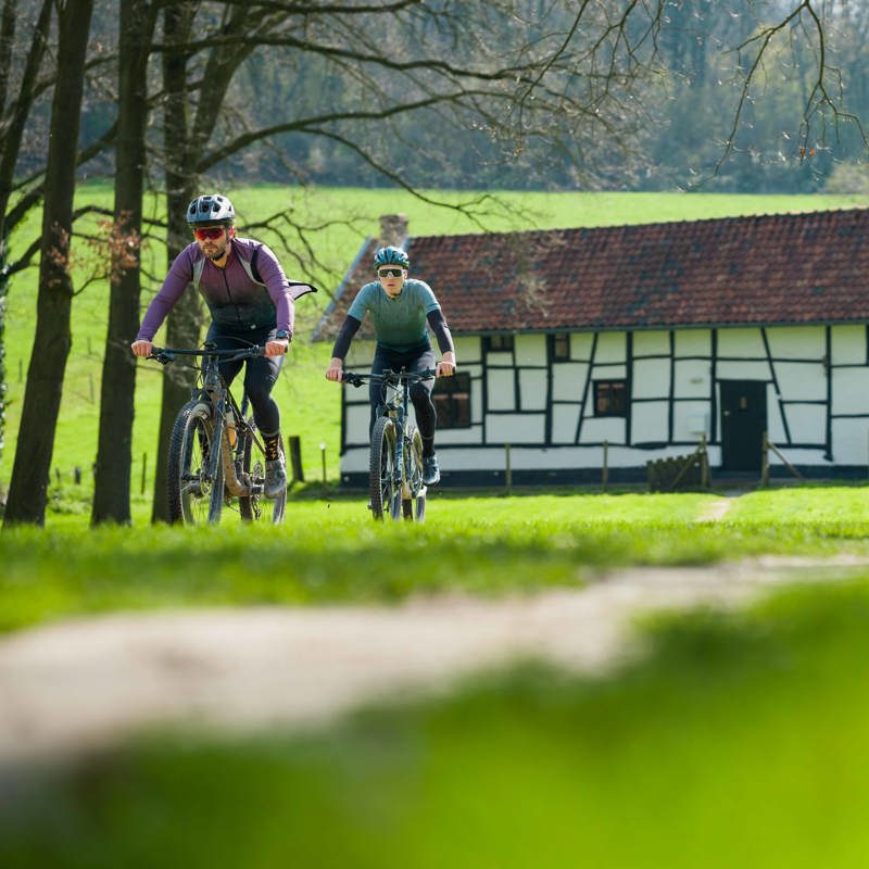 Twee mountainbikers fietsen langs een vakwerkhuis midden in de natuur