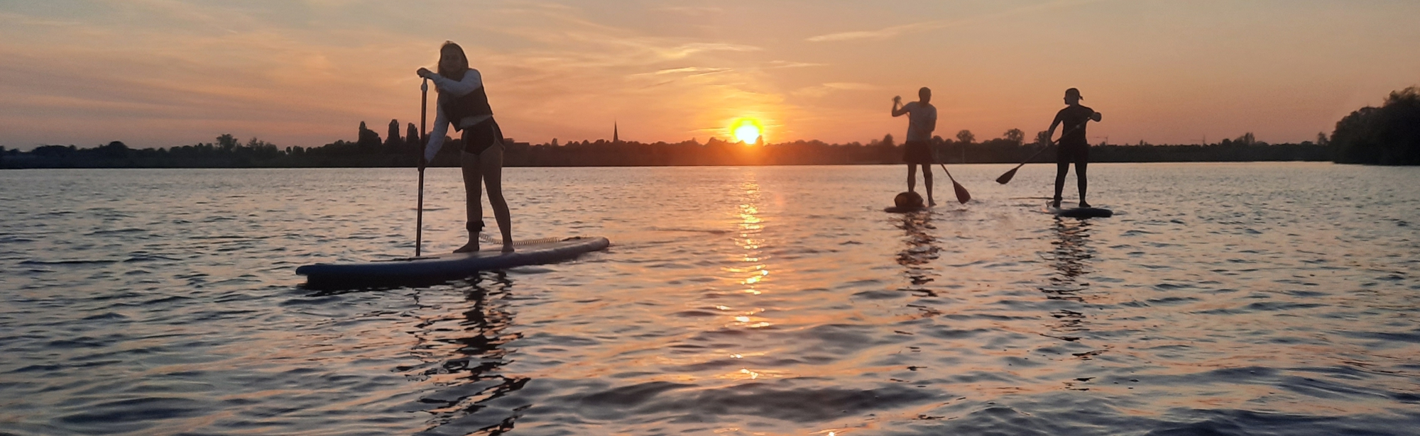 3 mensen op supboards tijdens ondergaande zon