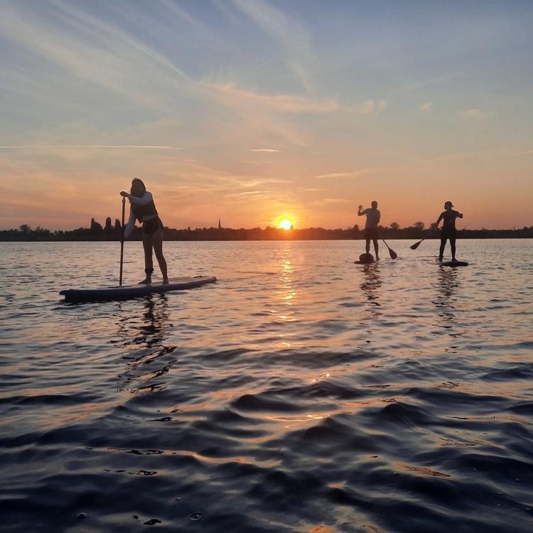 3 mensen op supboards tijdens ondergaande zon