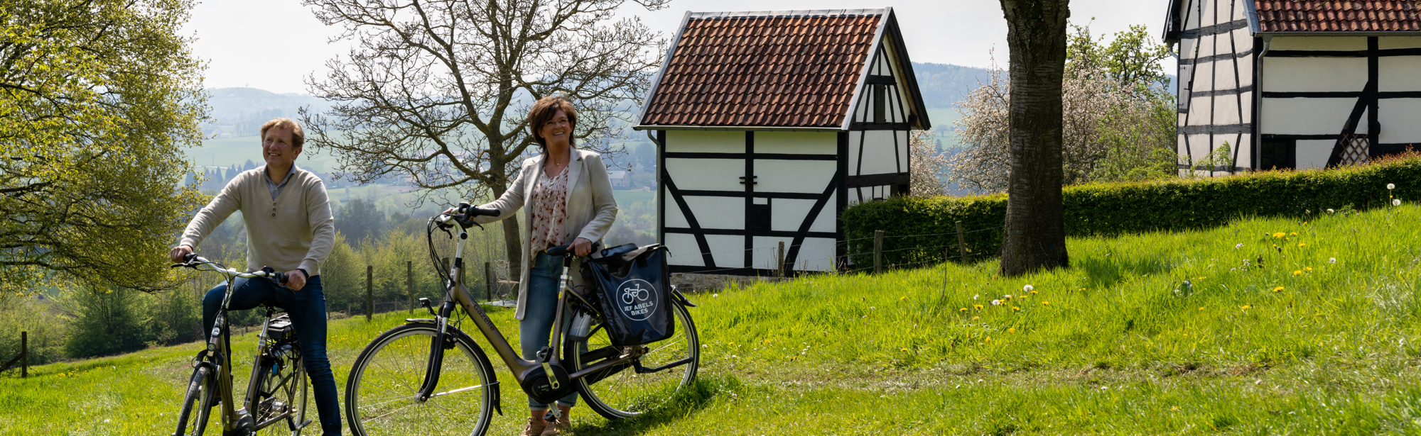 Twee fietsers staan in een weiland met vakwerkhuisjes