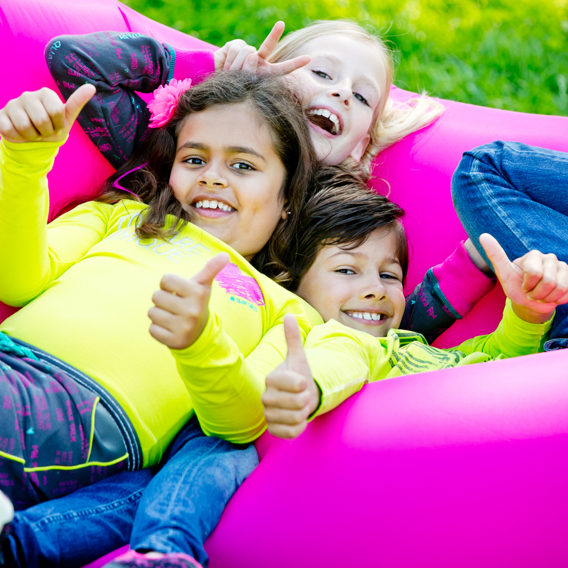 Drie kinderen liggen op een zitzak in het gras en steken hun duim op. 