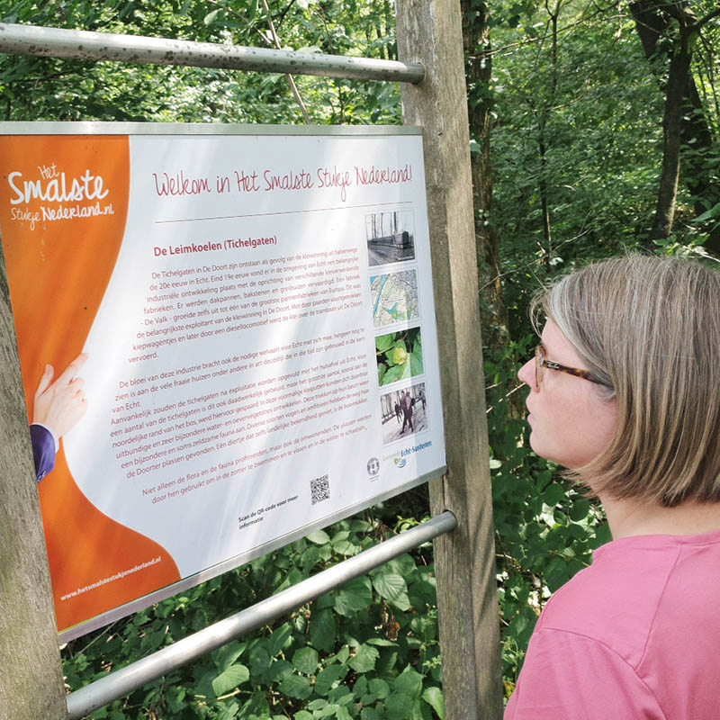 Wandelboswachter Ellen kijkt op een infobord bij De Doort