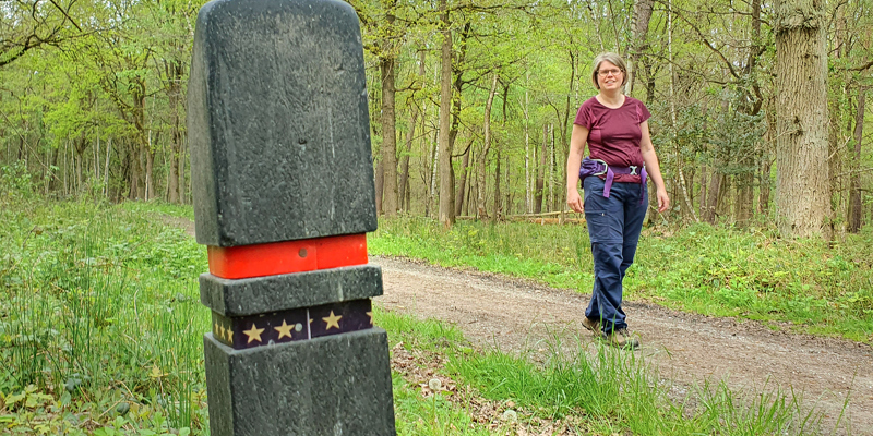 Boswachter Ellen wandelt langs een routepaaltje met 5 sterren in de Schinveldse Bossen