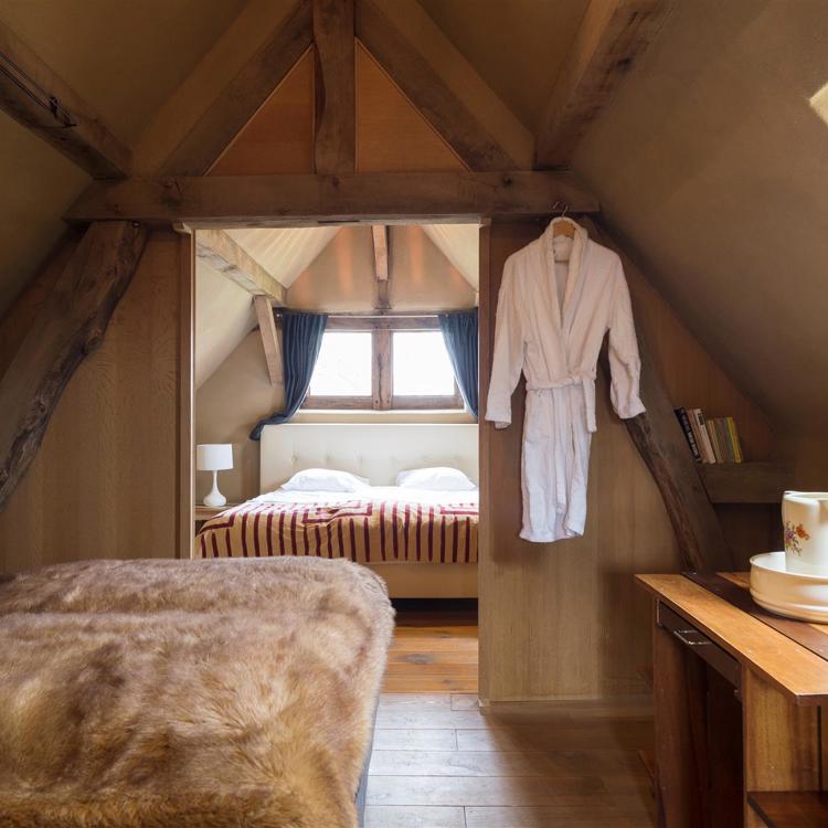 Een zolderkamer met warme dekens, een ochtendjas die aan de muur hangt en een tweepersoonsbed