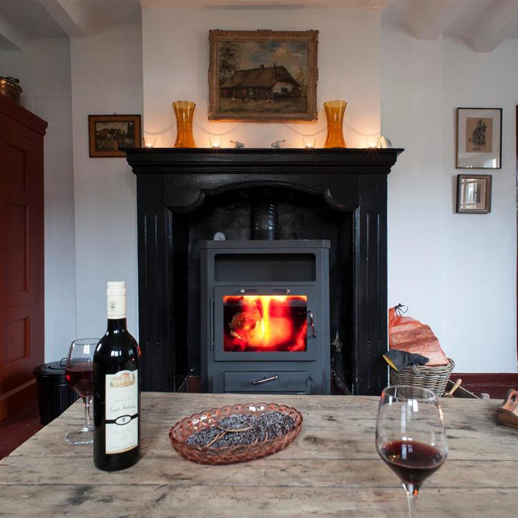 Een openhaard in een knusse ruimte met een fles rode wijn en twee volle wijnglazen