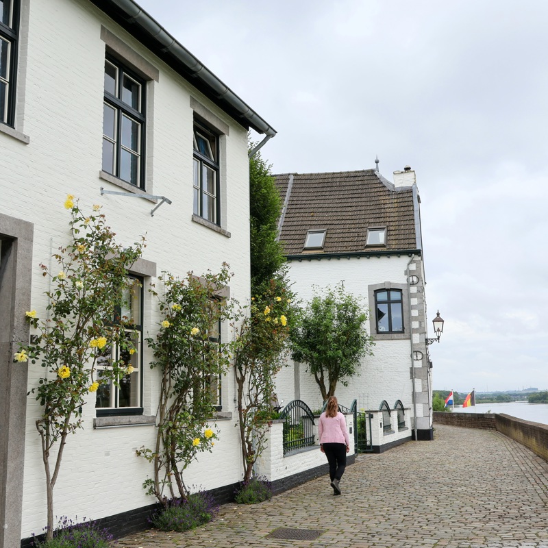 Dame wandelt langs de kade in Eijsden met mooie witte huizen.