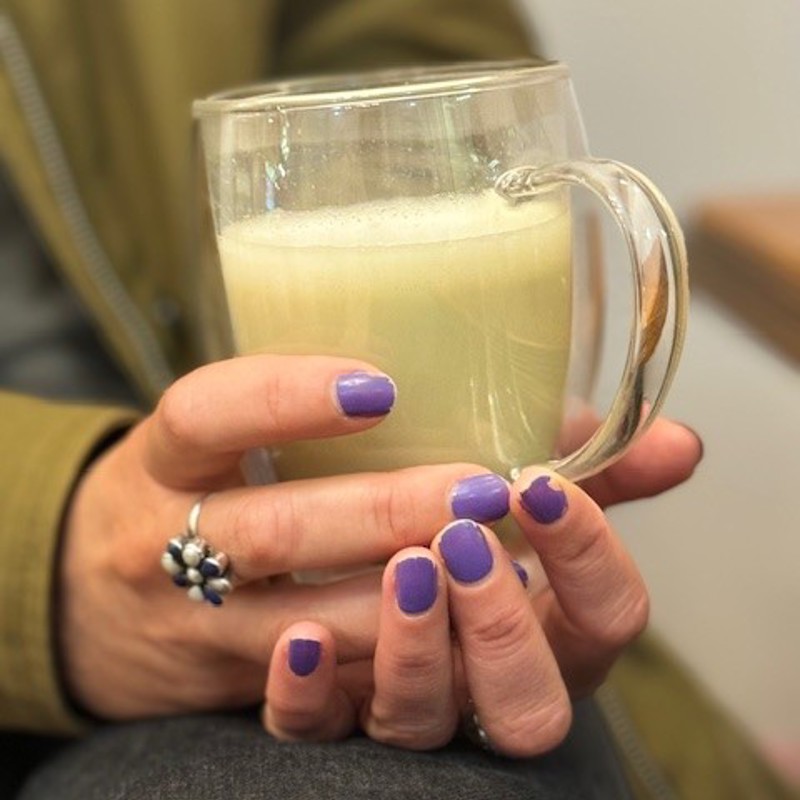 Hand met een kopje matcha latte in een doorzichtig glas