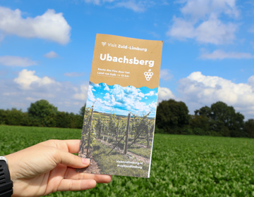 Blogger houdt wandelbrochure van Ubachsberg omhoog met de natuur op de achtergrond. 