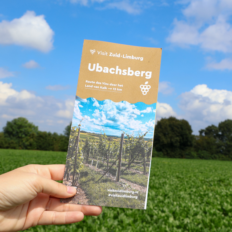 Blogger houdt wandelbrochure van Ubachsberg omhoog met de natuur op de achtergrond. 