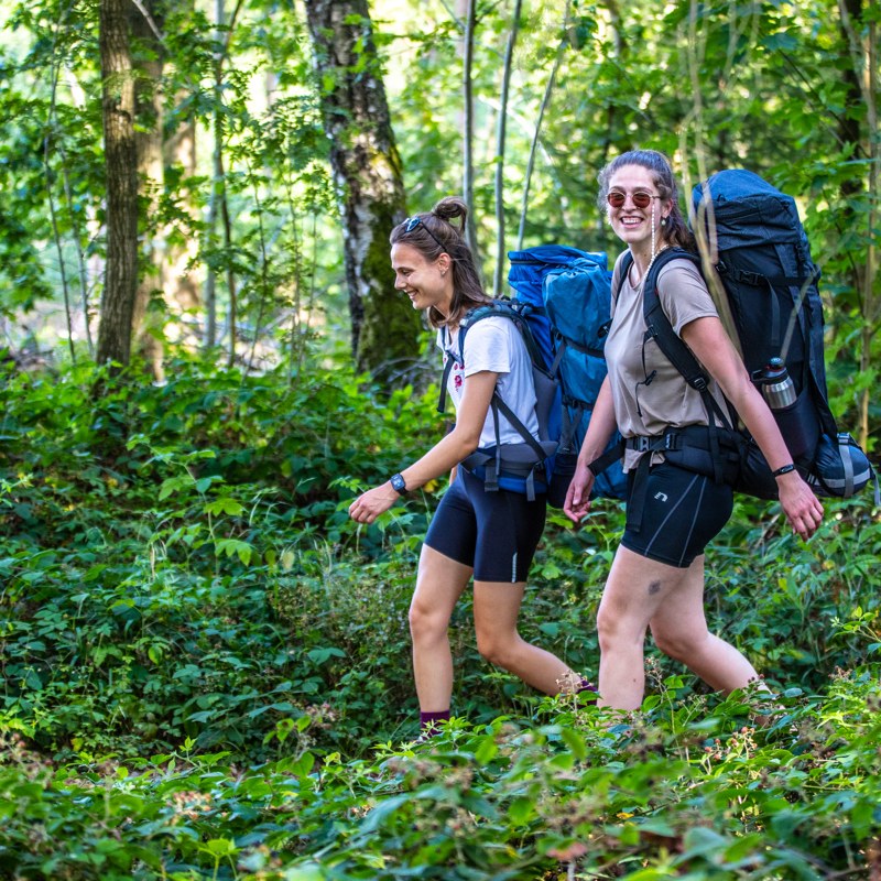 Twee meiden met backpack en wandeloutfit wandelen lachend door het bos