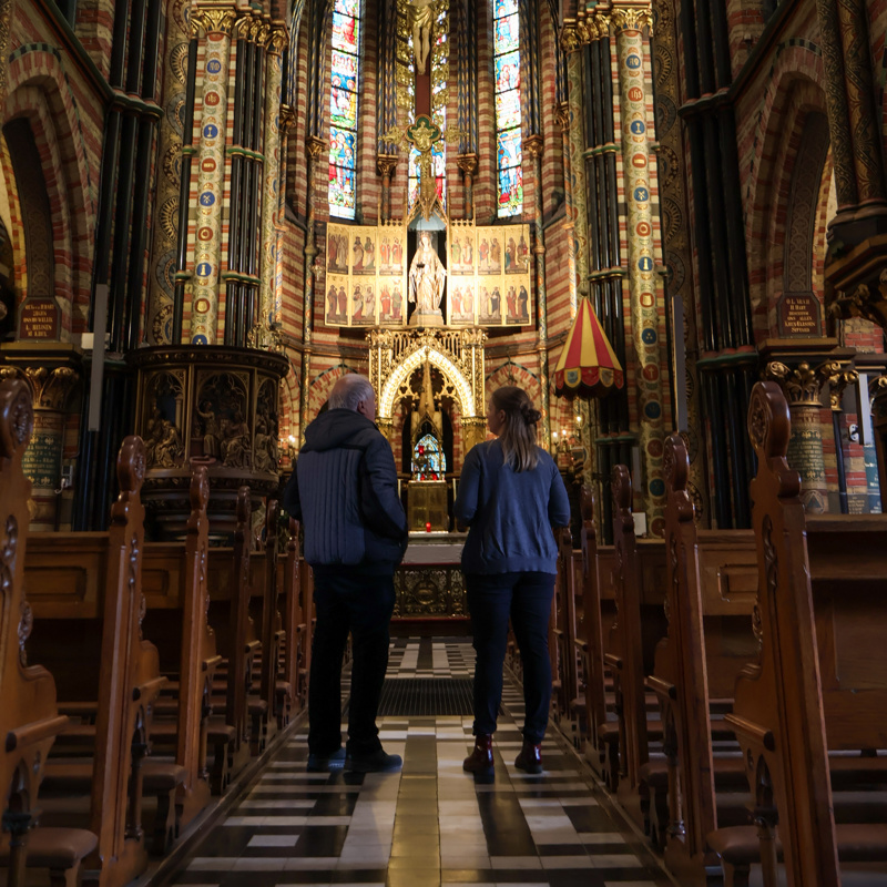 Twee personen staan in de gang van de kerk tussen de banken in. 