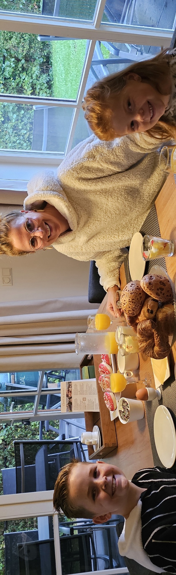 Een moeder en twee kleine kinderen zitten aan tafel van hun vakantiehuisje voor een lekker ontbijtje