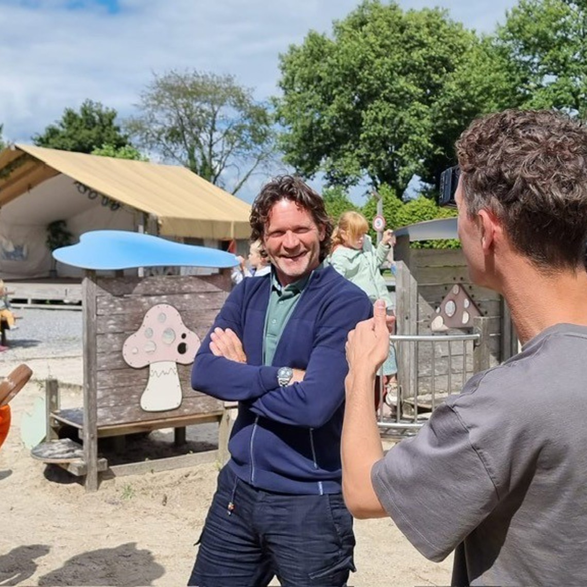 Sander Janson voor de camera met een oranje mascotte van de camping in Gulpen naast hem. 