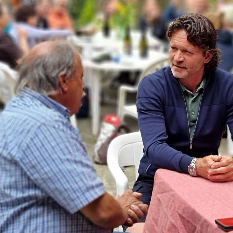 Sander zit aan tafel met iemand van Domaine Salamander, met flessen wijn op tafel. 