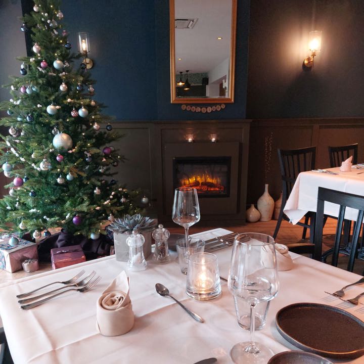 Gedekte tafel in restaurant met een kerstboom en openhaard op de achtergrond.