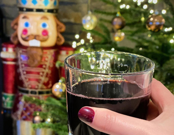 een glaasje glühwein met kerstboom en lampjes op de achtergrond