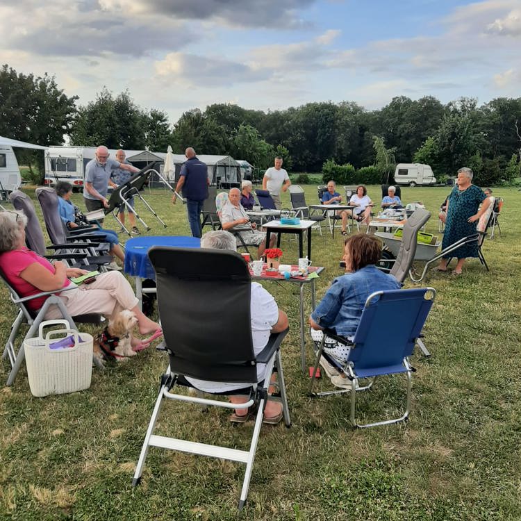 Een hoop campinggasten verzamelen zich bij elkaar met tafels en stoelen. 