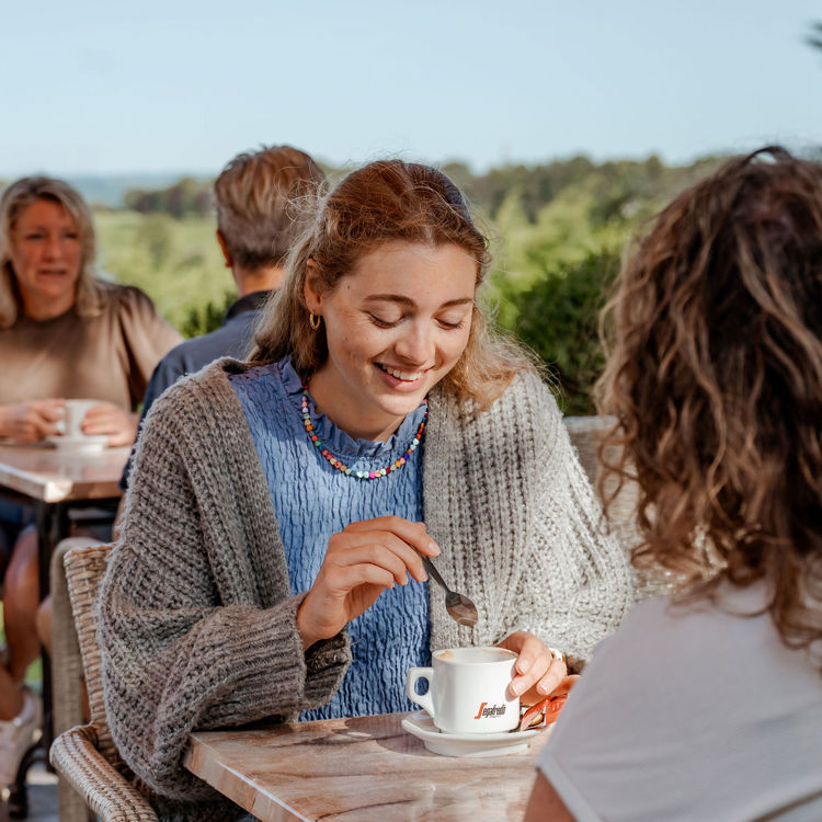 Vrouw drinkt koffie op het terras met uitzicht over het limburgse heuvelland.