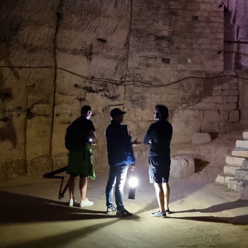 Drie personen staan in de ondergrondse grotten van Valkenburg en verlichten de ruime met een lantaarn. 