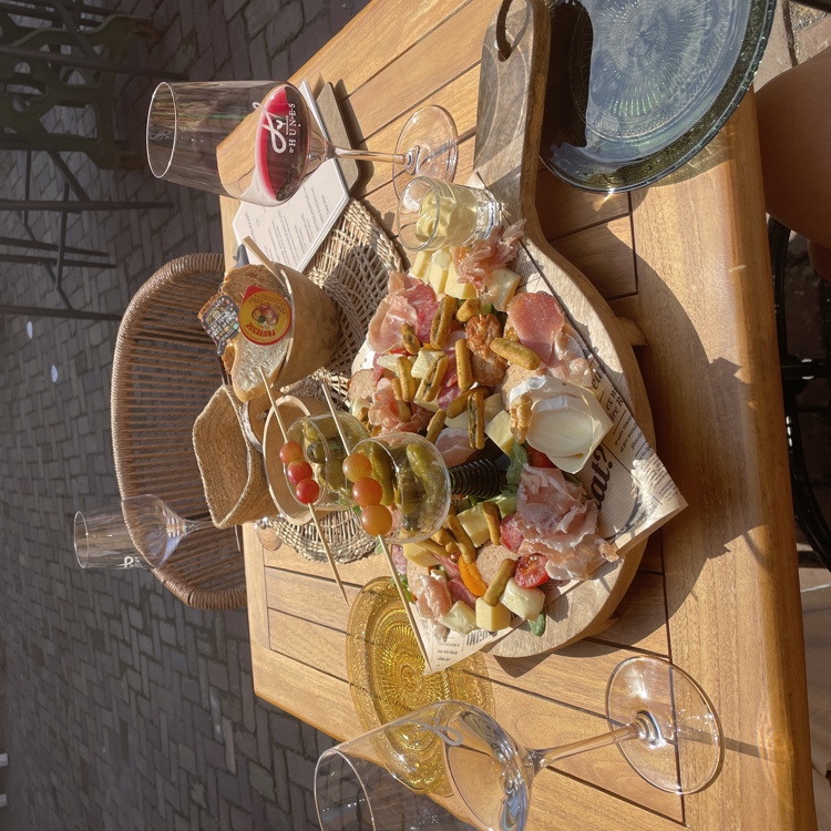 Een goed gevulde borrelplankje met twee glazen wijn op een zonnig terras