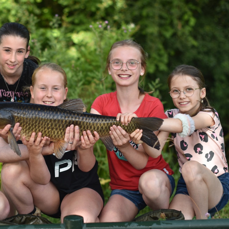 Kinderen met een begeleider houden grote gevangen vis in de handen en poseren voor de camera.