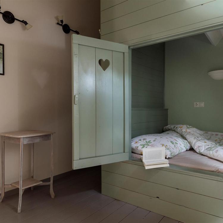 Bedstee in mintgroene kleur met een opgemaakt bed en een boek. 