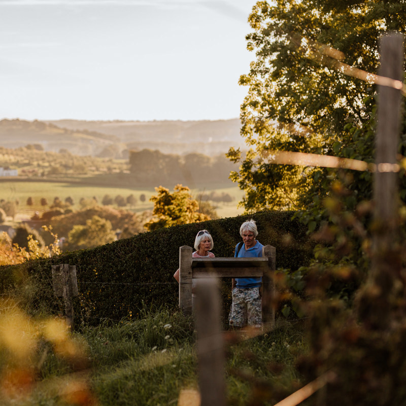 Twee wandelaars lezen het wijnbord van Wijngoed Aldenborgh met Toscaans uitzicht over de heuvels