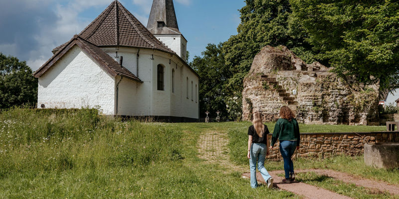 Twee dames wandelen richting een klein wit kerkje. 