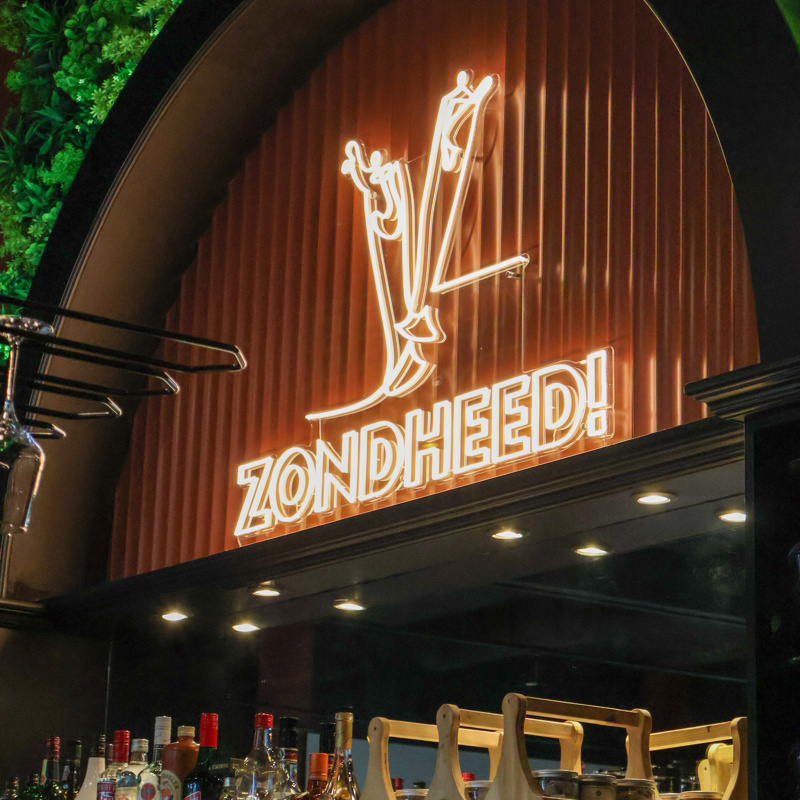 Bar met flessen drank en groot een lichtgevend logo van Brasserie Zondheed.