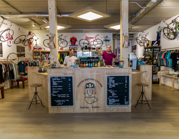 Koffiebar en merchandise in een wielercafé met twee medewerkers achter de bar.