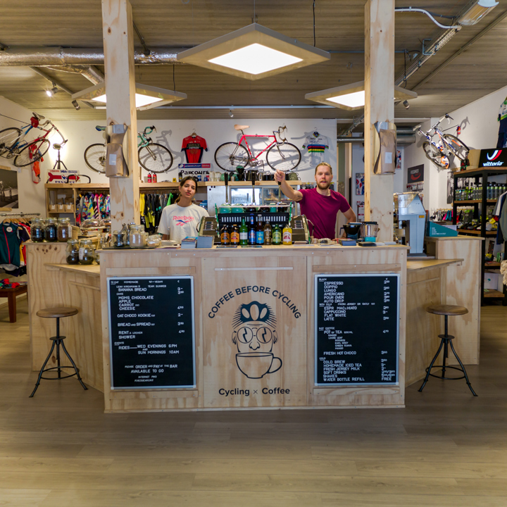 Koffiebar en merchandise in een wielercafé met twee medewerkers achter de bar.