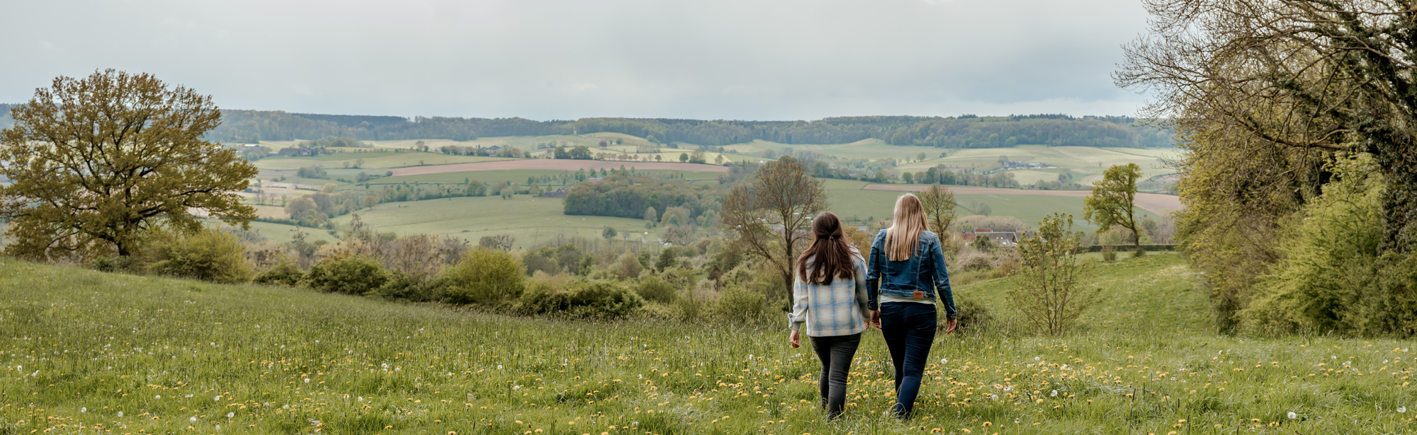 2 dames aan het wandelen in een veld met bloemen en het heuvelland op de achtergrond