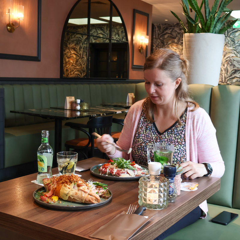 Blogger zit aan tafel met twee lunchgerechten op tafel. 