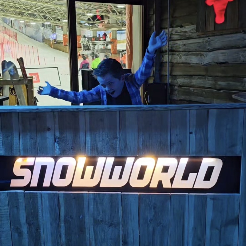 Jongetje steekt handen in de lucht achter houten schutting van snowworld. 