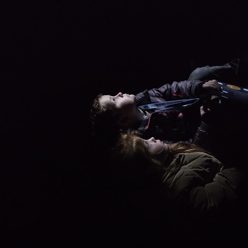 Twee kindjes kijken vol aandacht naar rechts in een donkere omgeving. 