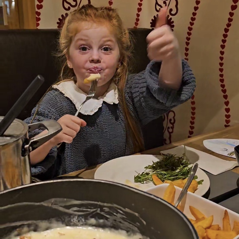 meisje steekt duim in de lucht achter de kaasfondue. 