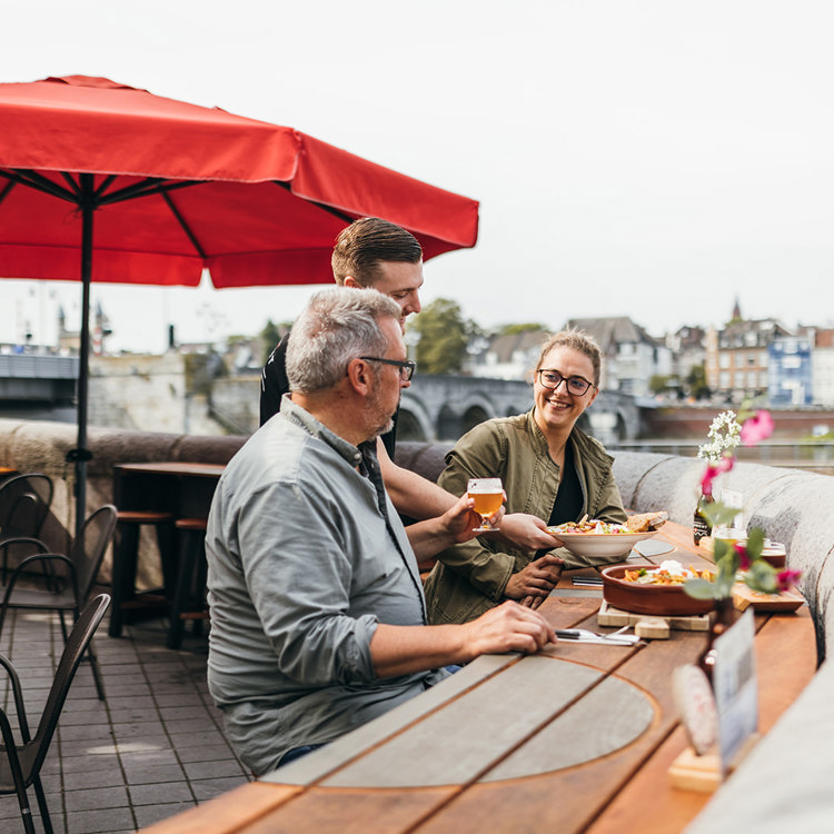 Twee mensen op het terras van Stadsbrouwerij Maastricht krijgen een pilsje en streekproducten aangeboden